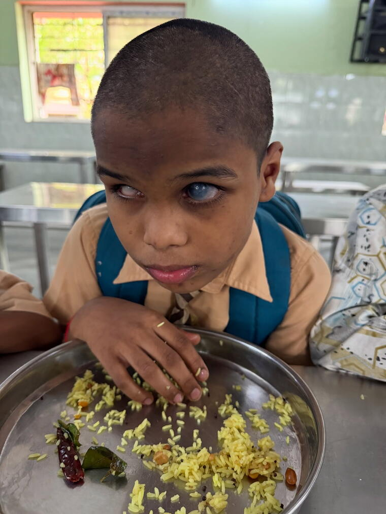 A young boy with severe visual impairment eating a meal of rice from a steel plate at his school