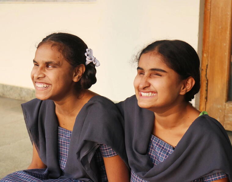 Two schoolgirls with visual impairments laughing together in their school uniforms